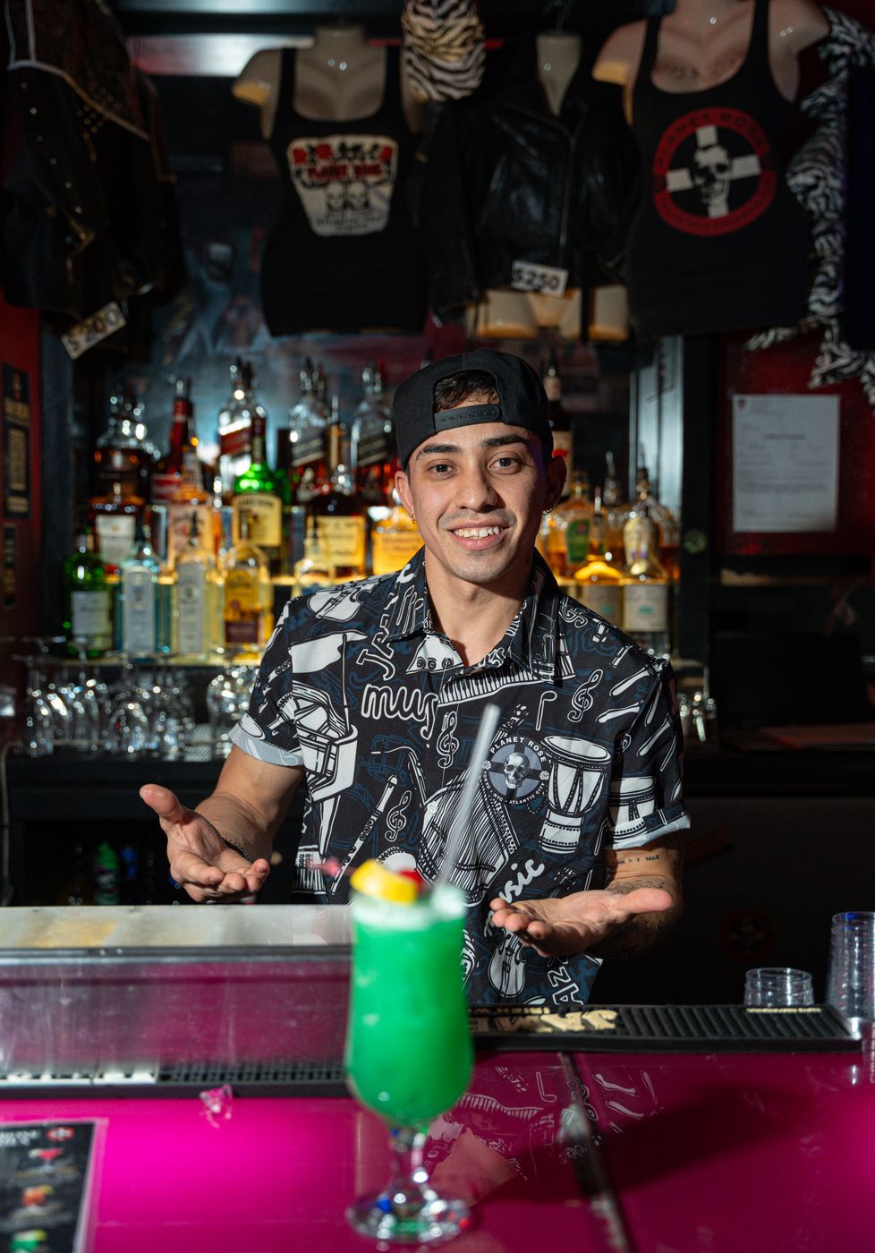 Smiling Planet Rose bartender serving a bright green cocktail on the pink bar