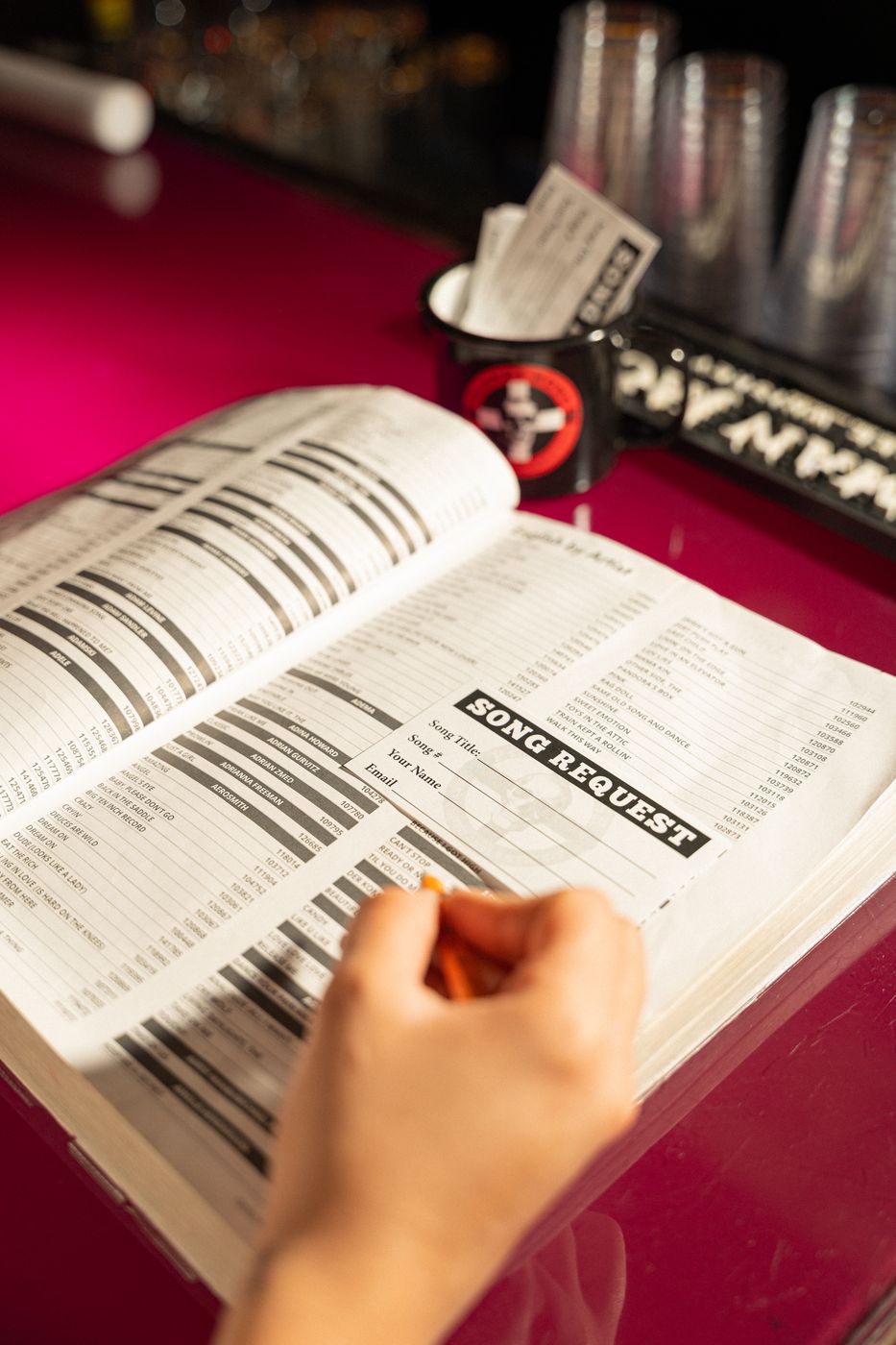 A hand filling out a song request slip on the open Planet Rose songbook